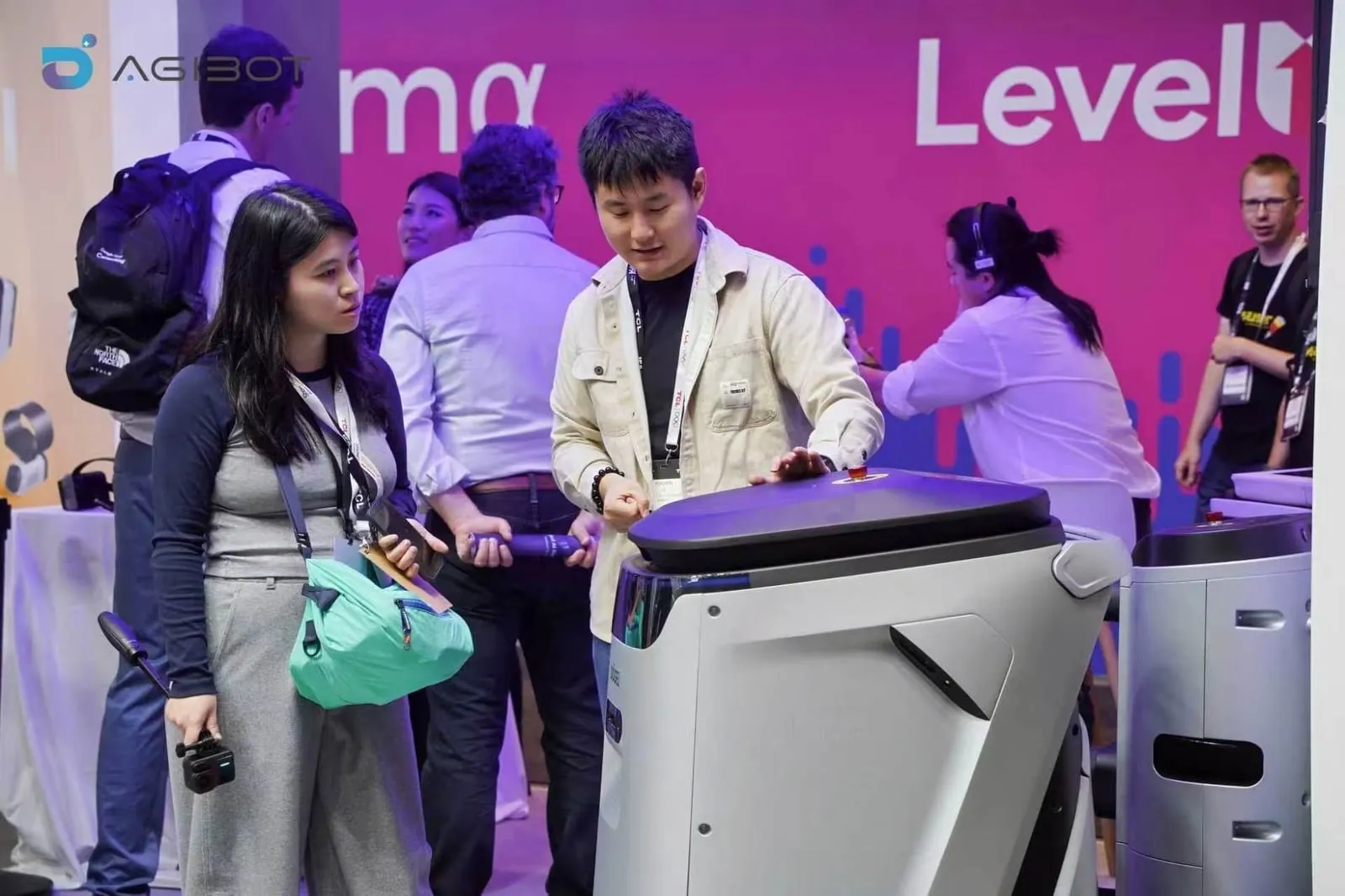 A visitor talking with the AGIBOT team next to a cleaning robot at the IFA 2026 booth